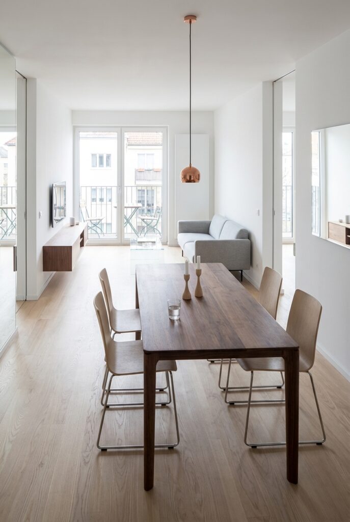 Kleines Wohnzimmer mit offenem Esstisch Neva aus Nussbaum, der mittig platziert ist